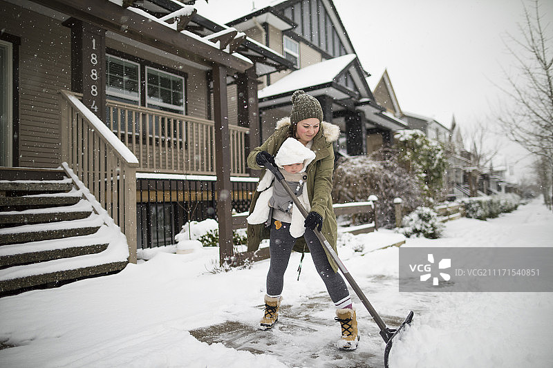 母亲和儿子在婴儿背带里在冬天在郊区铲雪图片素材