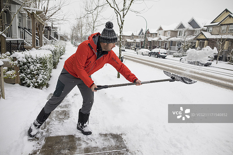 冬季郊区，男子在人行道上铲雪的侧面照图片素材