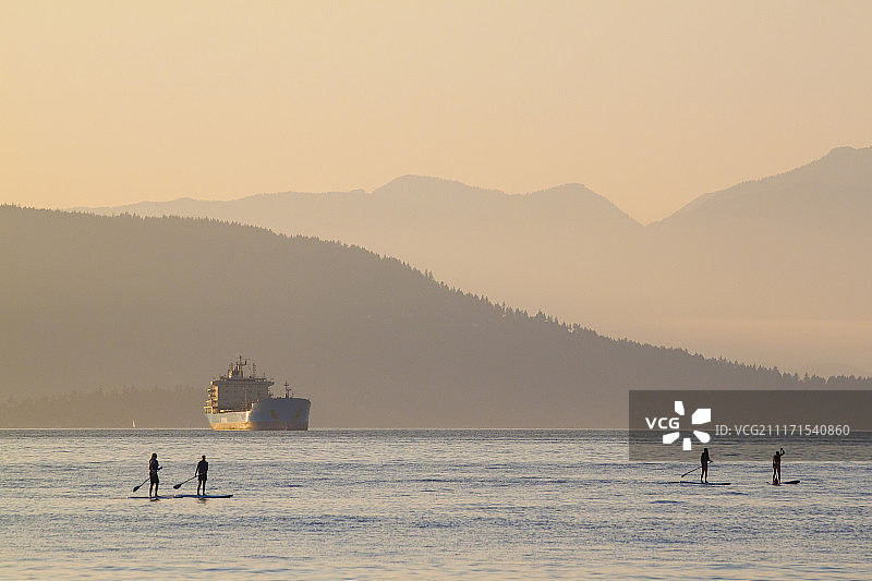 加拿大不列颠哥伦比亚省温哥华日落时在海上划桨板的四个人图片素材