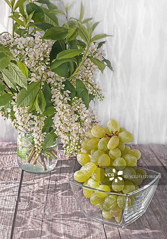 清晨阳光下透明玻璃容器中桌上的一束白葡萄图片素材