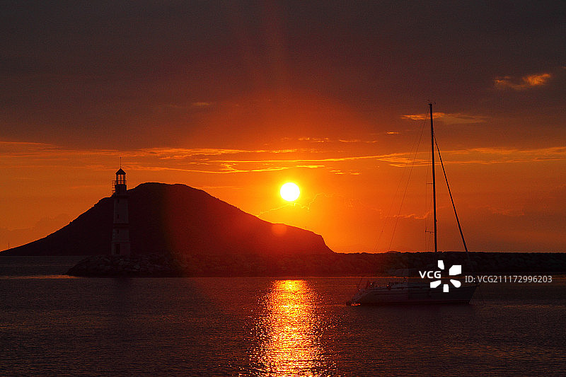 日落时分海边山丘和灯塔的轮廓图片素材