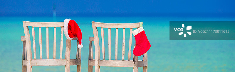 热带白色海滩椅子上的红色圣诞袜和圣诞帽图片素材