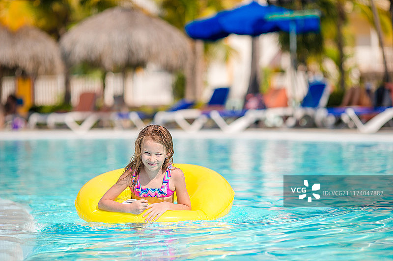 在豪华酒店室外游泳池里带着充气游泳圈玩耍的小女孩图片素材