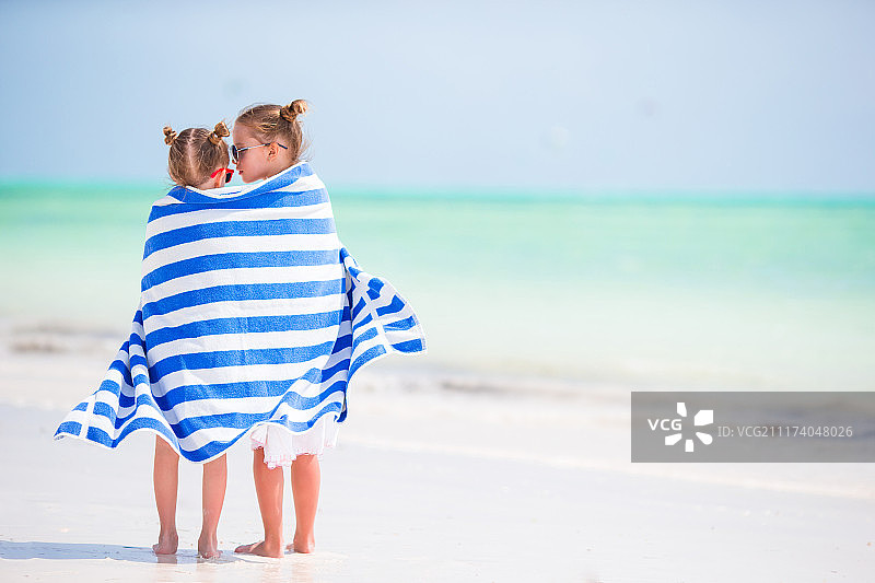在热带海滩上裹着毛巾的可爱小女孩，海滩度假的孩子们图片素材