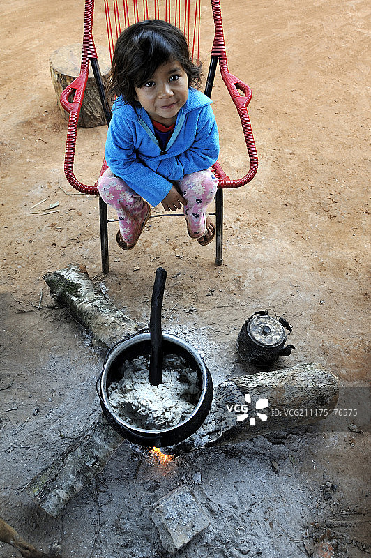 瓜拉尼印第安社区中坐在火炉旁喝粥的5岁女孩图片素材