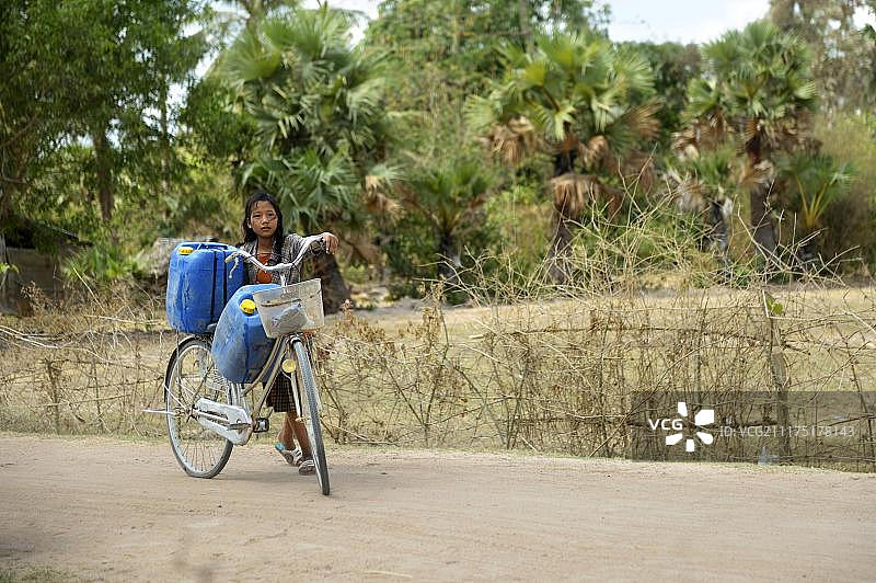 女孩用自行车从水库运送两个水罐图片素材