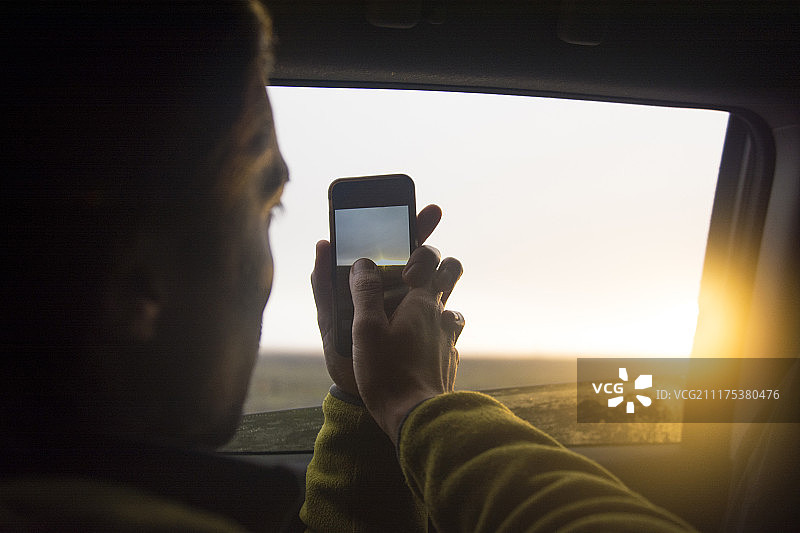 在冰岛东部霍芬，男子透过车窗用手机拍摄日落图片素材