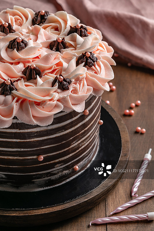 生日巧克力蛋糕与粉红色奶油鲜花在木制背景与蜡烛竖版照片图片素材