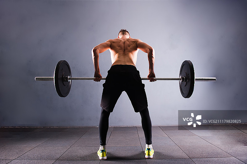 一位英俊的男人赤膊举起杠铃。健身房的Crossfit健身大重量杠铃锻炼图片素材