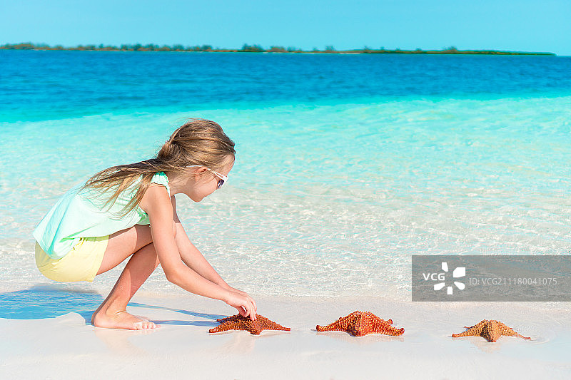 可爱的小女孩在白色空旷的沙滩上照顾红色海星图片素材