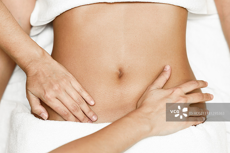 用手按摩女性腹部。治疗师对自己施加压力。俯视图的手按摩女性腹部。治疗师在腹部施加压力。在水疗沙龙接受按摩的女人图片素材