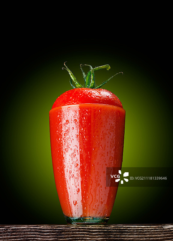 盛满番茄汁的湿玻璃杯，上面放着一块西红柿，摆在木桌上图片素材