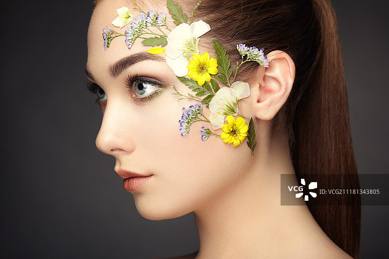 鲜花装饰的美丽女性面部特写：精致妆容，时尚美妆，睫毛，眼影图片素材