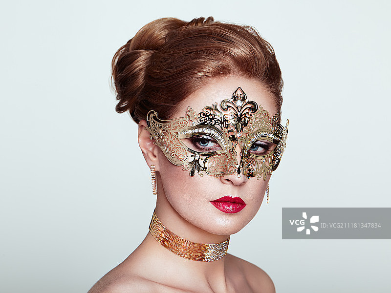 派对上戴着威尼斯狂欢节面具的美丽女人，白色背景。圣诞节和新年庆祝活动。化着节日妆容和红唇的性感女人。金色面具图片素材