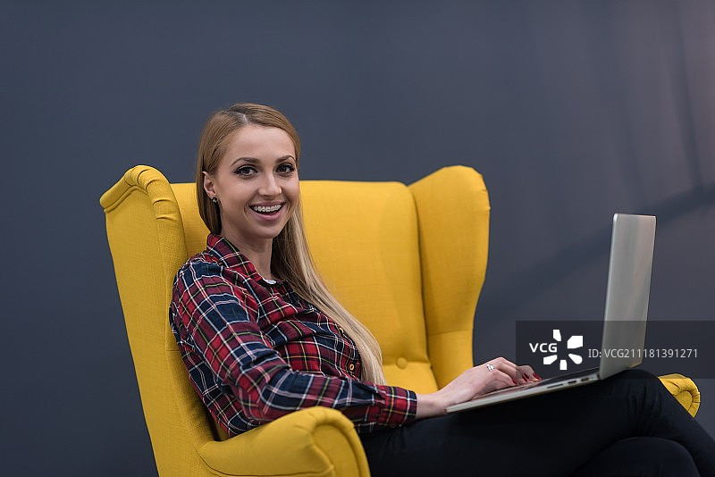 创业，女人在现代办公室用笔记本电脑工作，坐在黄色创意扶手椅上图片素材