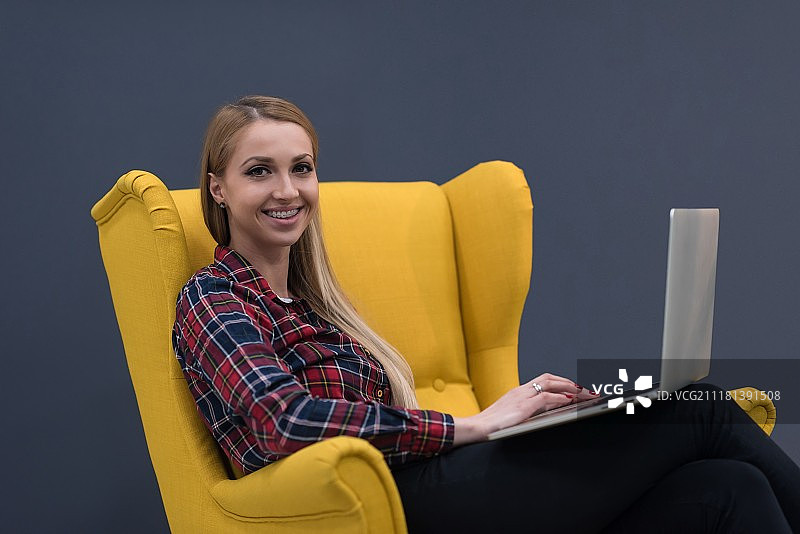 创业，女人在现代办公室用笔记本电脑工作，坐在黄色创意扶手椅上图片素材