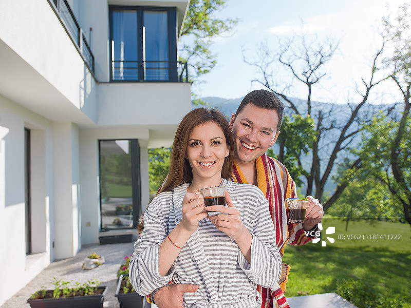 年轻漂亮的情侣穿着浴袍在豪华别墅前享受早晨的咖啡图片素材