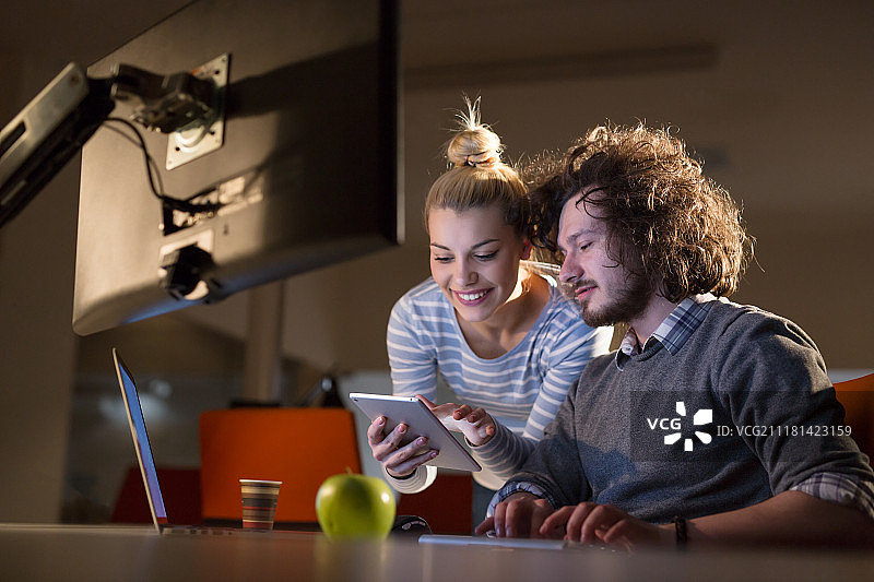 两名年轻的设计师正在利用现代科技在夜间办公室里设计一个新项目图片素材