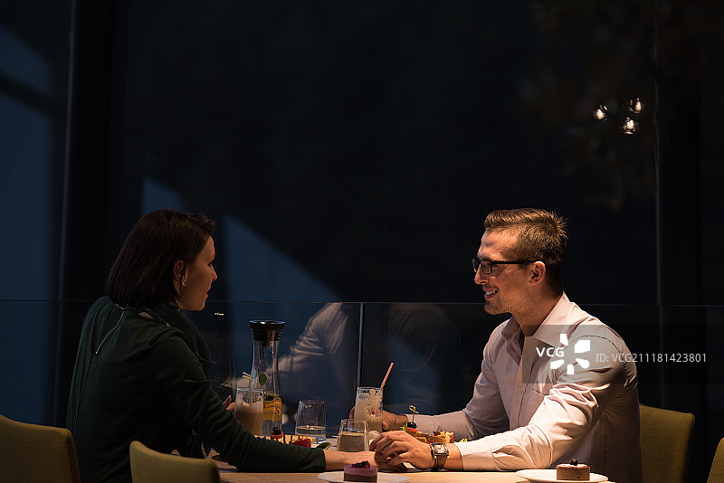 情侣在餐厅靠窗位置享用浪漫晚餐，庆祝情人节图片素材