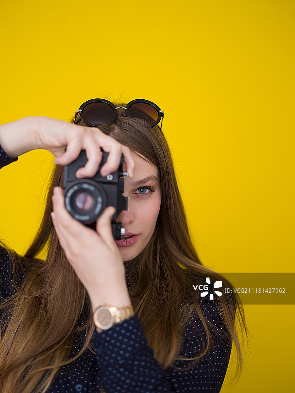 在黄色背景下用复古相机拍照的微笑漂亮女孩肖像图片素材