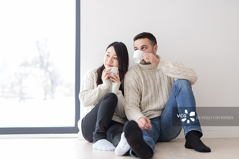 快乐的年轻多元民族情侣在寒冷的冬日在家中靠窗享用早咖啡图片素材
