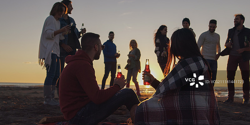 在海滩篝火旁喝啤酒的快乐年轻朋友们图片素材