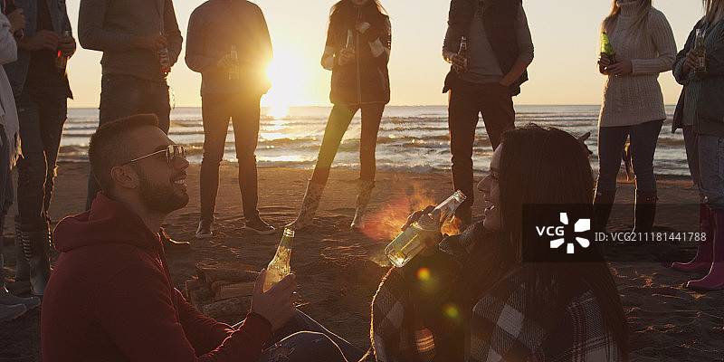 在海滩篝火旁喝啤酒的快乐年轻朋友们图片素材