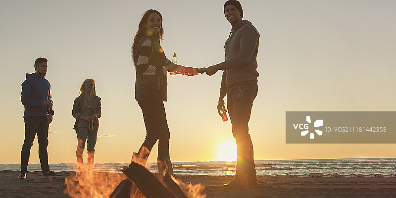 在海滩篝火旁喝啤酒的快乐年轻朋友们图片素材