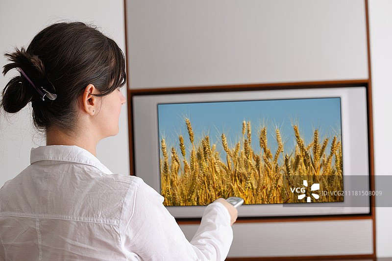 快乐的年轻女人在现代家居客厅看电视图片素材