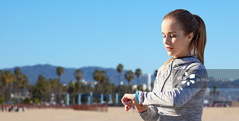 运动、人物与科技概念：女子佩戴健身追踪器在加利福尼亚威尼斯海滩训练图片素材