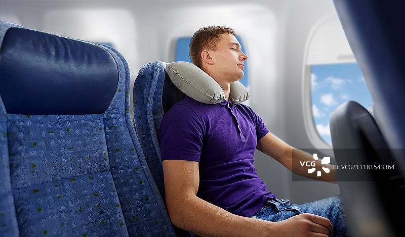 青年男子在飞机上用充气枕睡觉图片素材