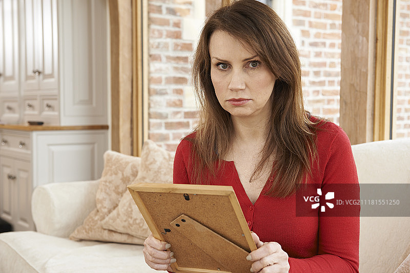 不快乐的中年妇女看着相框里的照片图片素材