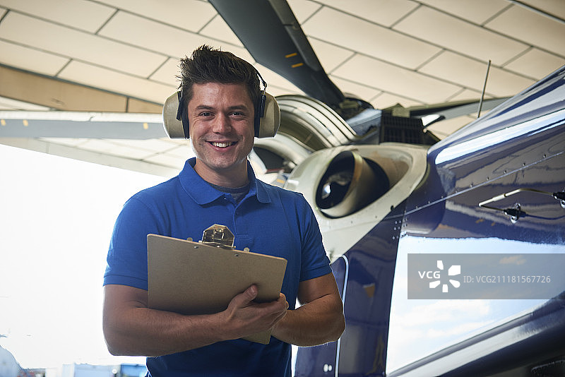 拿着剪贴板在机库中检查直升机的男性航空工程师 портрет 照片图片素材