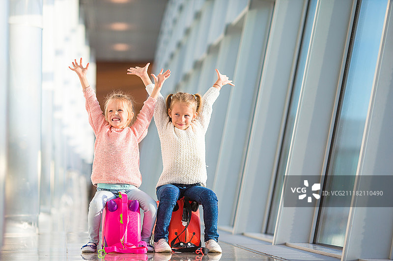在机场坐在行李箱上等待登机的可爱小女孩图片素材