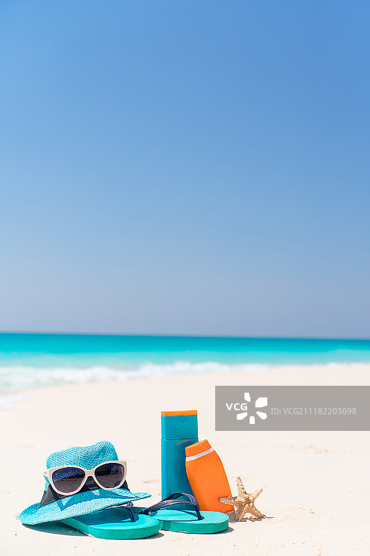 白色沙滩背景上的防晒霜瓶、泳镜、海星和太阳镜图片素材