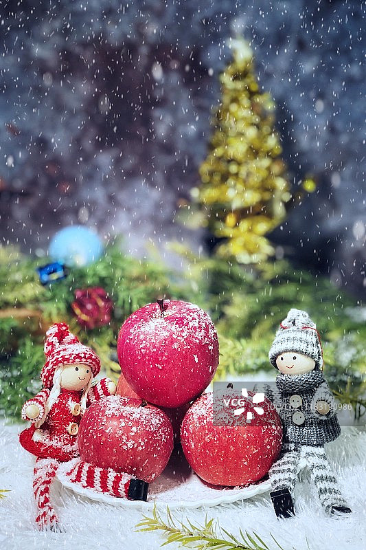 雪花中围着红苹果的两个人偶图片素材