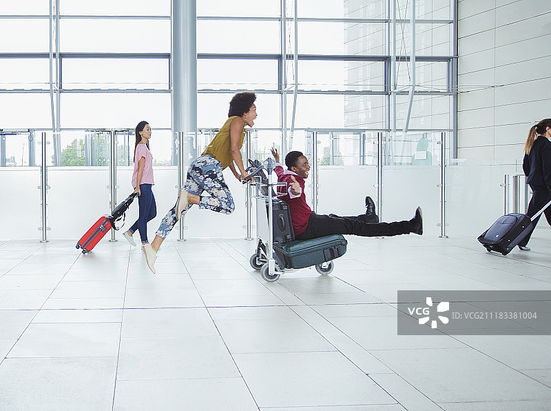 嬉戏的情侣在机场推着行李车图片素材