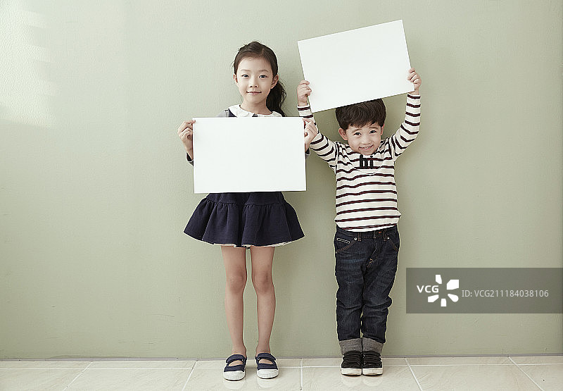 女孩和小男孩站在墙前举着白色横幅的摄影照片图片素材