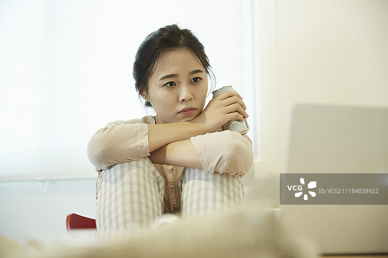 女子在桌前一边吃鸡一边喝啤酒，同时看笔记本电脑的照片图片素材