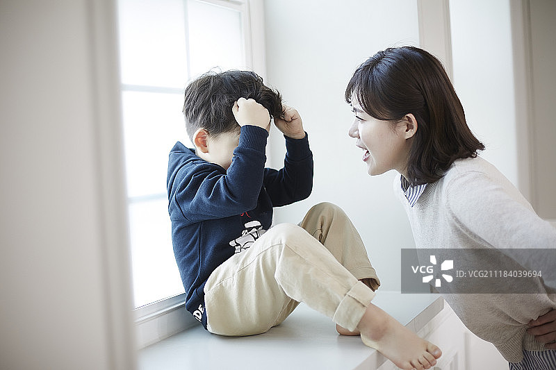 母亲生气地看着坐在窗边的小儿子的照片图片素材