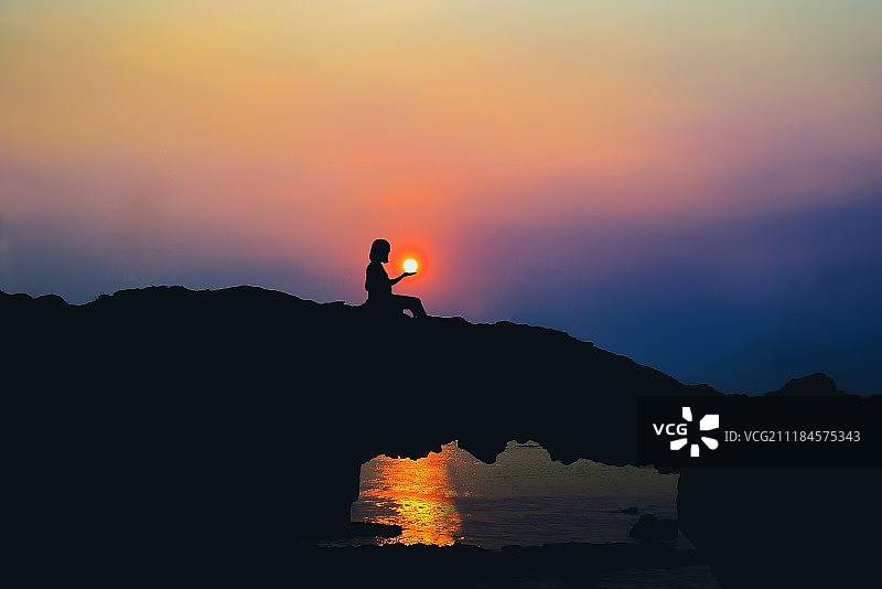 女人在日落时分在海边摆出托着太阳的姿势图片素材