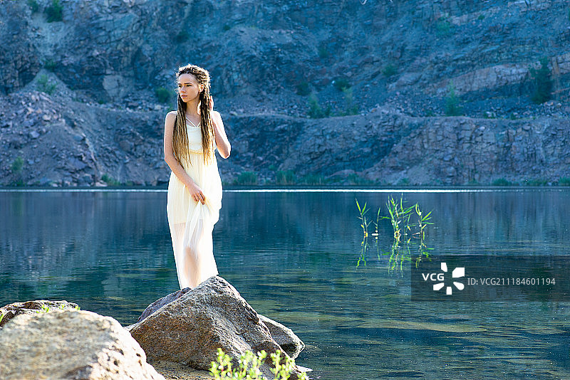 一位穿着白色连衣裙，留着脏辫的美丽女孩站在日出时的湖边图片素材