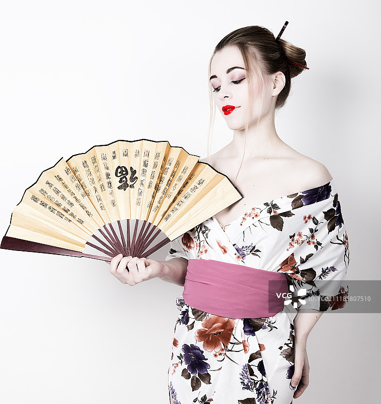装扮成艺伎的美丽女孩，手持中国风扇，精致的艺伎妆容和发型图片素材