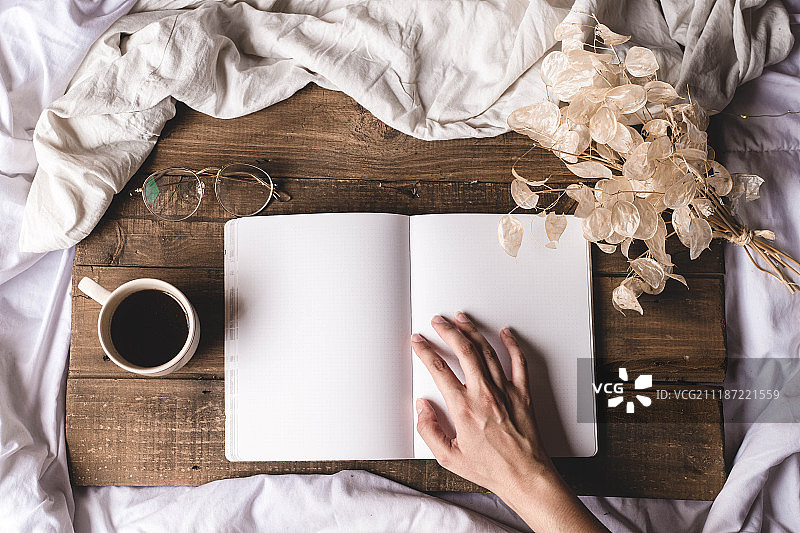 手在触摸木板上的书，旁边有眼镜和干花图片素材