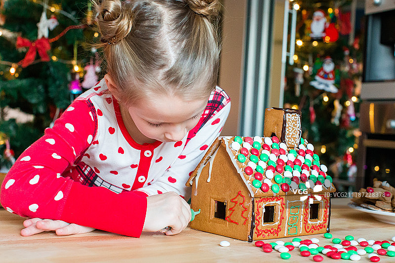 小女孩们在装饰好的客厅壁炉旁制作圣诞姜饼屋图片素材