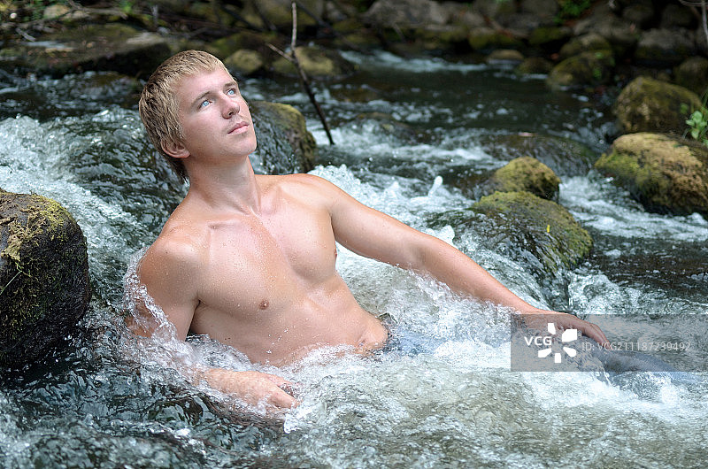 年轻男人躺在岩石间湍急的河流中休息图片素材
