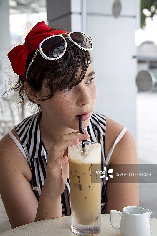 在咖啡馆里用吸管喝冰咖啡的雀斑少女图片素材