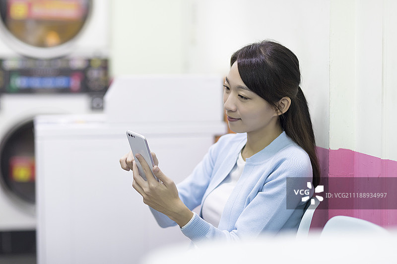 在洗衣间用手机的年轻女人图片素材