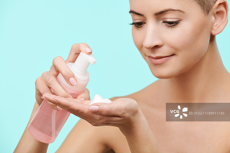 30多岁的笑容满面的中年妇女使用温和的泡沫洁面乳图片素材