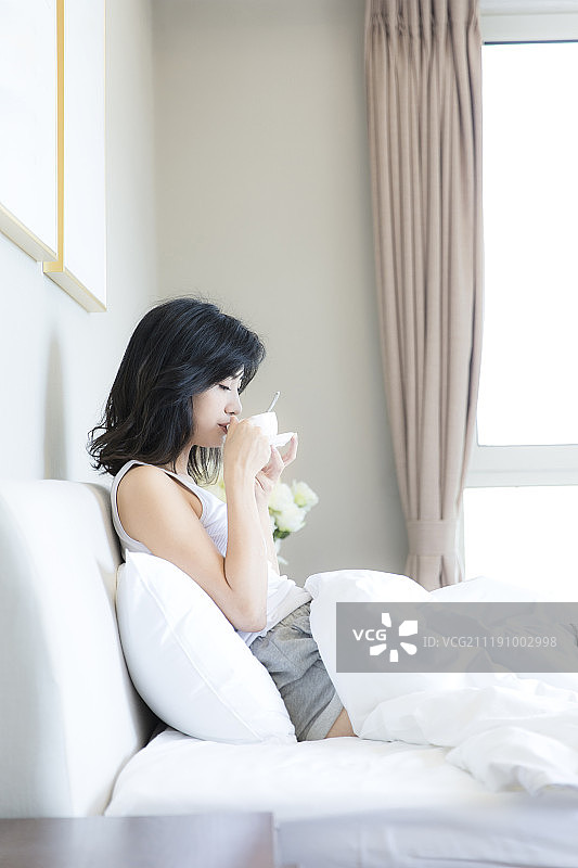 年轻女子在卧室床上喝咖啡图片素材